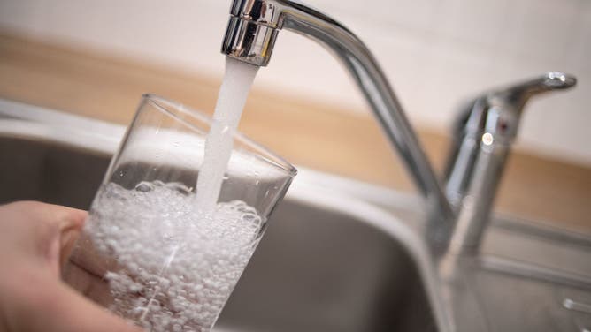 A man holds a glass under a running tap.