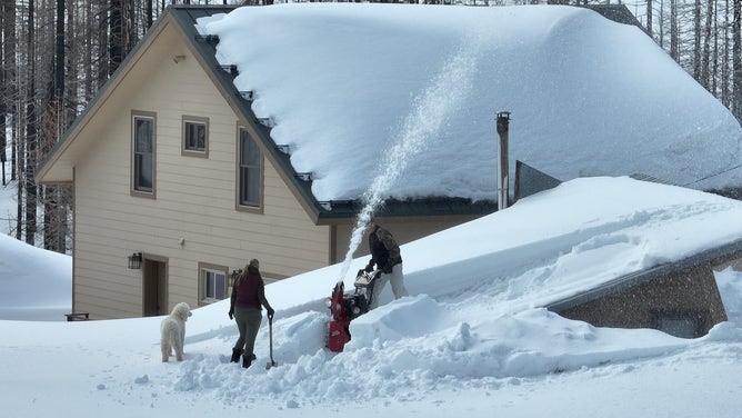 TWIN BRIDGES, CALIFORNIA - MARCH 20: In an aerial view, residents are seen using a snow blower to clear snow from the room of a home on March 20, 2023 in Twin Bridges, California. The Lake Tahoe region is preparing for more snow in the coming days after seeing near record levels of snow so far this season. California continues to be impacted by atmospheric river events that are pummeling the state with heavy rains, high winds and snow.