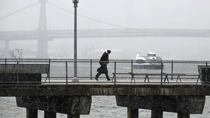 A person walks during rain and snow before the New York city skyline in Brooklyn on March 14, 2023. - A major Nor'easter is expected to bring heavy snow and strong winds to the East Coast on Wednesday, forecasters say.