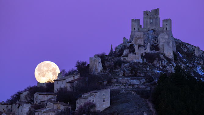 Full moon sets behind Rocca Calascio castle and village (LAquila), Italy, on March 7, 2023. March full moon is also known as the worm moon, because it coincides with the time of year when earthworms begin to emerge from the thawing soils.