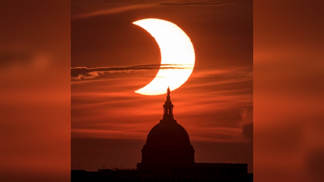 FILE - In this handout image provided by NASA, a partial solar eclipse is seen as the sun rises behind the Capitol Building on June 10, 2021 in Arlington, Virginia.