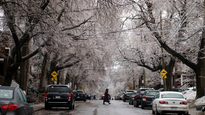 A person crosses the street as iced-over tree branches are seen after freezing rain hit parts of Quebec and Ontario in Montreal, Canada, on April 5, 2023.