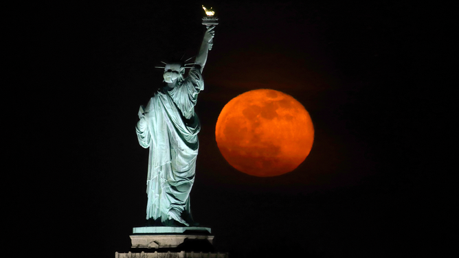 FILE - The pink moon rises next to the Statue of Liberty in New York City a day after being full on April 27, 2021 as seen from Jersey City, New Jersey.