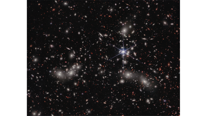Bright white sources surrounded by a hazy glow are the galaxies of Pandora’s Cluster, a conglomeration of already-massive clusters of galaxies coming together to form a megacluster. The concentration of mass is so great that the fabric of spacetime is warped by gravity, creating an effect that makes the region of special interest to astronomers: a natural, super-magnifying glass called a 