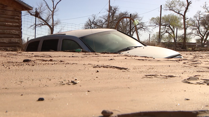 A car partially submerged under mud and dirt.