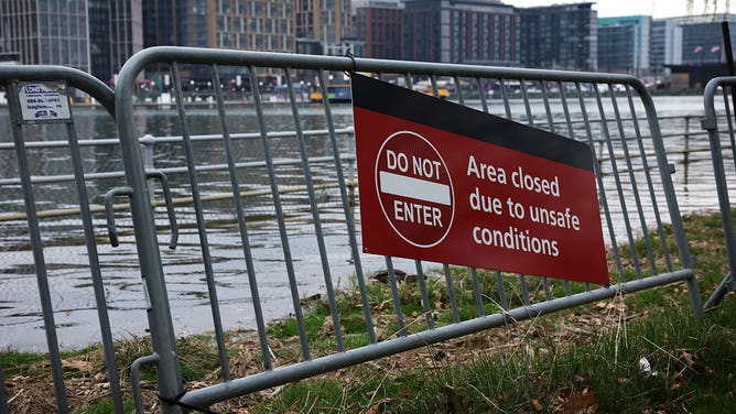 A "Do Not Enter" sign is on display as floodwaters wash up the bank during high tide across the Washington Channel from The Wharf amid cherry blossoms in peak bloom near the Tidal Basin on March 23, 2023, in Washington, D.C.