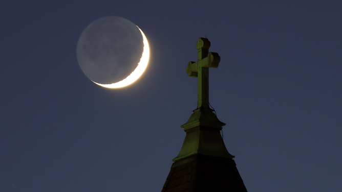 FILE - A 9 percent waxing crescent moon lit with earthshine sets behind a church on December 25, 2022, in Jersey City, New Jersey.