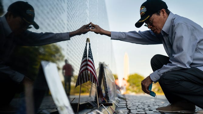 Quyen Pham, of Newport News, Va., pauses after placing a lit cigar at the base of the marble wall of the Vietnam Veterans Memorial to pay his respects on Memorial Day as the sunsets over the National Mall, on Monday, May 31, 2021.