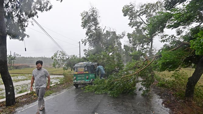 A man walks past a fallen tree on power lines in Teknaf on May 14, 2023, during the Cyclone Mocha's landfall. Cyclone Mocha crashed ashore in Myanmar and southeastern Bangladesh on May 14, uprooting trees, scattering flimsy homes in Rohingya displacement camps and bringing a storm surge into low-lying areas.