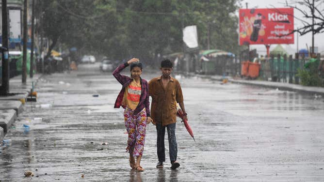 Pedestrians walk in an empty street under the rains after Cyclone Mocha's crashed ashore, in Kyauktaw in Myanmar's Rakhine state on May 14, 2023. Cyclone Mocha crashed ashore in Myanmar and southeastern Bangladesh on May 14, 2023, uprooting trees, scattering flimsy homes in Rohingya displacement camps and bringing a storm surge into low-lying areas.