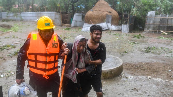 The volunteer helped an old woman move to take shelter in the Cyclone Shelter in Shahpori island on the outskirts of Teknaf, on May 14, 2023, ahead of Cyclone Mocha's landfall.