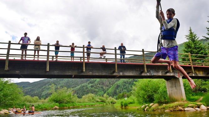 A boy swings out over the Roaring Fork River near the North Star Nature Preserve on July 1, 2021 in Aspen, Colorado. 