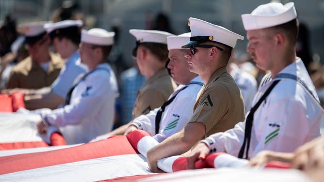 US Marines and US Navy sailors hold a large American flag as it is unfurled during the Intrepid Sea, Air & Space Museum’s annual Memorial Day Commemoration Ceremony on May 30, 2022 in New York City.