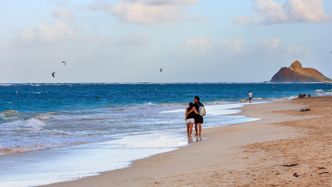 FILE - Couple Taking a romantic stroll at sunset along the sandy shoreline of Lanikai Beach with the Mokulua Islands in the distance.