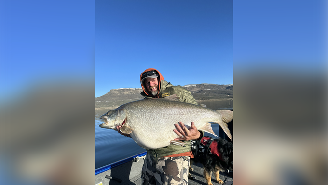 Scott Enloe hold his likely record-breaking catch. The lake trout he reeled in weighed 73.29 lbs.