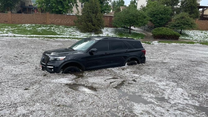 A black SUV stuck in floodwater in Colorado, as white hailstones float on the water's surface. June 21, 2023.