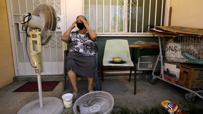 PACOIMA, CA - AUGUST 3, 2021 - - Felisa Benitez, 86, wipes the sweat from her brow while taking a break from cleaning her stand-up electrical fan on the porch of her home where temperatures reached 99 degrees at the San Fernando Gardens Public Housing in Pacoima on August 4, 2021. Benitez, who lives alone, tries to only use fan to cool herself even though she has an AC unit, to the right, at her place. She is on a limited budget and uses the AC sparingly to avoid a huge electrical bill that she cannot afford to pay. Benitez, who has lived at the gardens since the 90s, spends a great deal of her day seated in the shade of her porch. According to Los Angeles County Coroners and Medical Offices, hundreds of heat-related deaths reviewed by the Times showed the victims included seniors who died alone in apartments without air conditions, or with the thermostat off. (Genaro Molina / Los Angeles Times via Getty Images)
