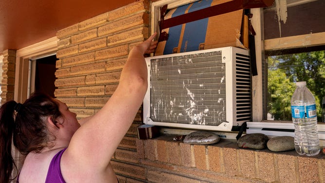 Woman tries to seal off her window air conditioning unit.