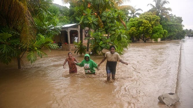 Residents cross the submerged Route Nationale 2 at L'Acul in the Arrondissement of Léogâne 23 mi (or 37 km) west of Port-au-Prince, Haiti, June 3, 2023, during heavy rains.