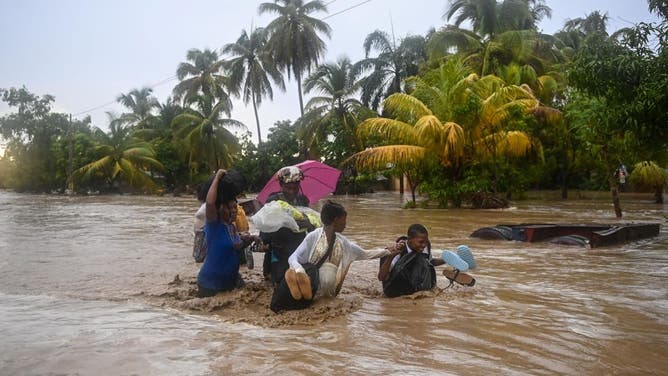 Residents cross the submerged Route Nationale 2 at L'Acul in the Arrondissement of Léogâne 23 mi (or 37 km) west of Port-au-Prince, Haiti, June 3, 2023, during heavy rains