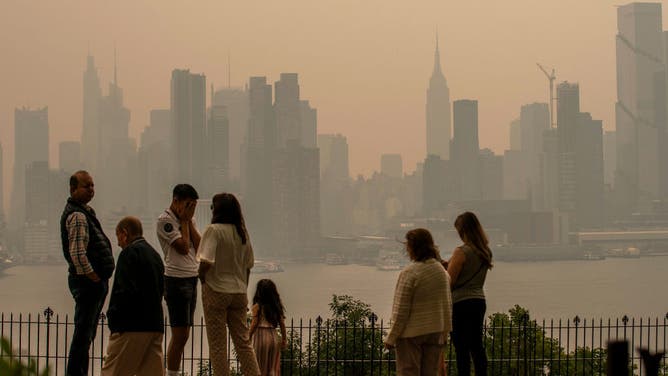 People stand in a park as the New York City skyline is covered with haze and smoke from Canada wildfires on June 7, 2023 in Weehawken, New Jersey. Air pollution alerts were issued across the United States due to smoke from wildfires that have been burning in Canada for weeks.