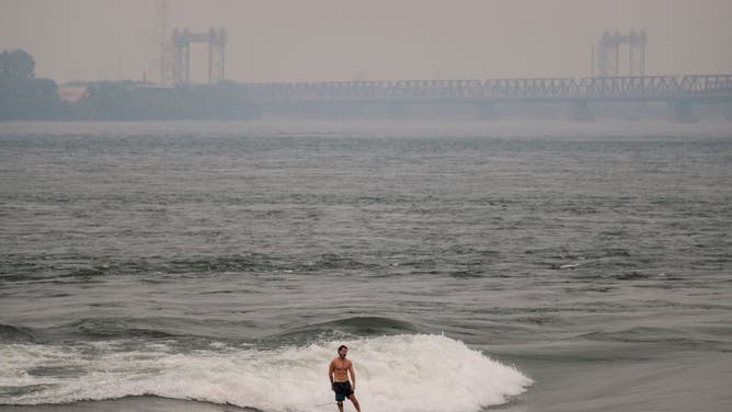 A man surfs in the St-Lawrence river with the smoke caused by the wildfires in Northern Quebec in the background in Montreal, Quebec, Canada on June 25, 2023.