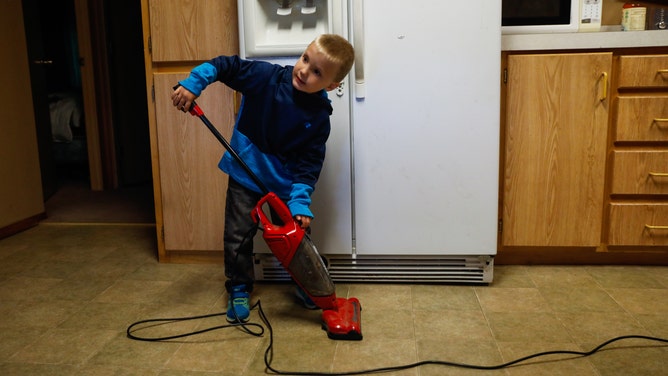 A young boy holds a vacuum cleaning in a kitchen.