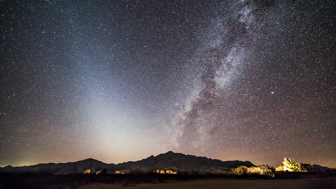 FILE - Depictions of two kinds of dust in space: At left the pyramid-shaped glow of Zodiacal Light caused by sunlight reflecting off interplanetary dust in the inner solar system from comets and meteoroids, while at right is the band of the bright Milky Way, made of stars in our galaxy But along it lie dark lanes of interstellar dust made of carbon compounds made in the atmospheres of stars and dispersed into the Galaxy.