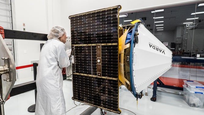 An employee looks at the Rocket Lab Photon spacecraft built for Varda Space Industries in the cleanroom