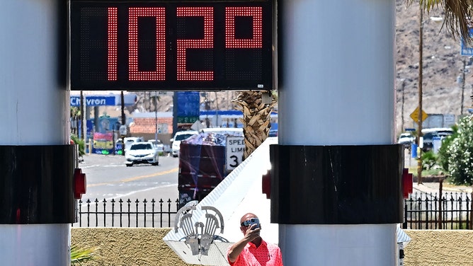 A man takes a selfie beside a thermometer showing 102 degrees farenheit in Baker, California on July 11, 2023, amidst a heat wave.