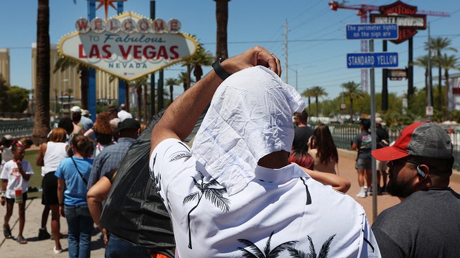 Satya Soviet Patnaik shields himself from the sun while waiting in line to take a photo at the historic Welcome to Las Vegas Sign during a heat wave in Las Vegas, Nevada, on July 14, 2023.