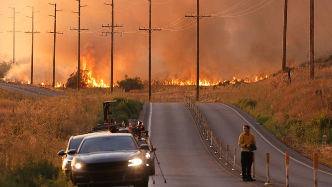A man stands in a road near flames of the Rabbit fire in Moreno Valley in Riverside County, Californian on July 14, 2023.
