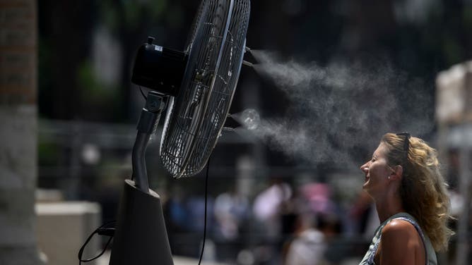 A woman cools down by a fan during an ongoing heat wave with temperatures reaching 44 degrees, at Colosseo area (Colosseum), on July 17, 2023 in Rome, Italy.
