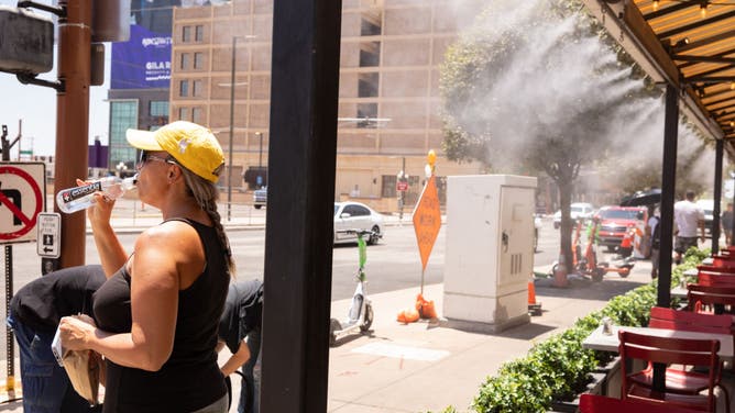 A resident drinks water while standing next to misters during a heat wave in Phoenix, Arizona, US, on Thursday, July 20, 2023. Phoenix extended its record streak of days above 110F to 20 on Wednesday with a high of 119F.