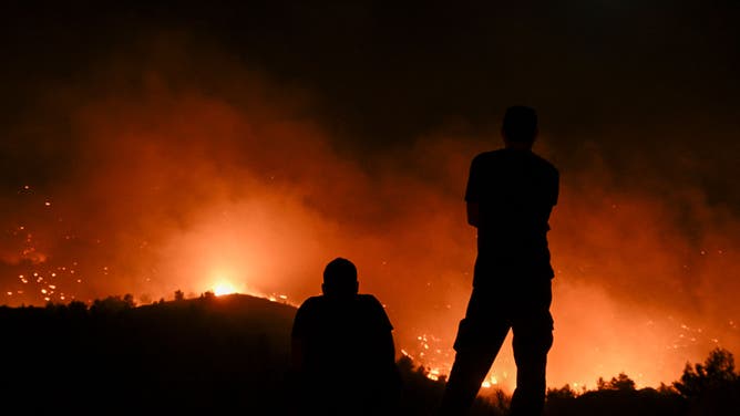 TOPSHOT - People watch the fires near the village of Malona in the Greek island of Rhodes on July 23, 2023. Tens of thousands of people fled wildfires on the Greek island of Rhodes on July 23, 2023, as terrified tourists scrambled to get home. Firefighters tackled blazes that erupted in peak tourism season, sparking the country's largest-ever wildfire evacuation -- and leaving flights and holidays cancelled.
