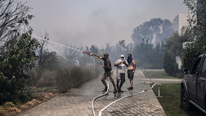 Civilians use a hose to attempt to stop a fire from approaching houses between the villages of Kiotari and Gennadi, on the Greek island of Rhodes on July 24, 2023. Firefighters tackled blazes that erupted in peak tourism season, sparking the country's largest-ever wildfire evacuation -- and leaving flights and holidays cancelled. Tens of thousands of people have already fled blazes on the island of Rhodes, with many frightened tourists scrambling to get home on evacuation flights.