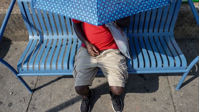 Yemichael Abebe uses an umbrella to take shelter from the sun while waiting for a bus on July 27, 2023 in Takoma Park, Maryland.