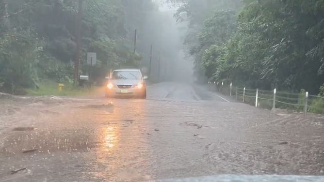A car is seen approaching a flooded roadway in Torrington, Connecticut, on Sunday, July 16, 2023.