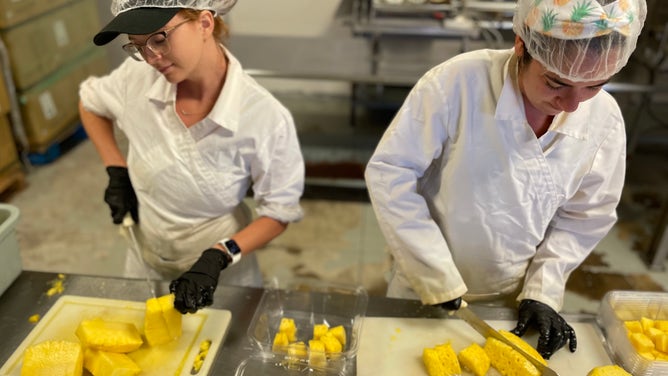Two women cut and package pineapples.