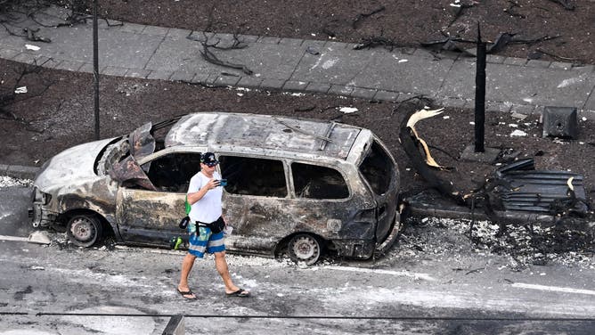 An aerial image taken on August 10, 2023 shows a person walking past a destroyed car in the aftermath of wildfires in western Maui in Lahaina, Hawaii. At least 36 people have died after a fast-moving wildfire turned Lahaina to ashes, officials said August 9, 2023 as visitors asked to leave the island of Maui found themselves stranded at the airport. The fires began burning early August 8, scorching thousands of acres and putting homes, businesses and 35,000 lives at risk on Maui, the Hawaii Emergency Management Agency said in a statement. (Photo by Patrick T. Fallon / AFP) (Photo by PATRICK T. FALLON/AFP via Getty Images)