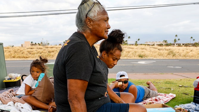 Maalaea, Maui, Thursday, August 10, 2023 - Noe Lopes sits with her granddaughter Leilani and great granddaughter Kawehi as the sun sets on their third day of waiting to return home near Lahaina. They and other evacuees camped in a parking lot along the Honoapiilani Highway, hoping to be allowed back into Lahaina, two days after a devastating wildfire tore through the community. (Robert Gauthier/Los Angeles Times via Getty Images)