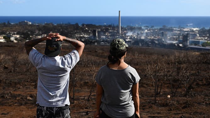 Maui residents John Rey Serrano and Lexie Lara look from a road above Lahaina Town in the aftermath of a wildfire in Lahaina, western Maui, Hawaii on August 11, 2023. A wildfire that left Lahaina in charred ruins has killed at least 67 people, authorities said on August 11, making it one of the deadliest disasters in the US state's history. Brushfires on Maui, fueled by high winds from Hurricane Dora passing to the south of Hawaii, broke out August 8 and rapidly engulfed Lahaina.