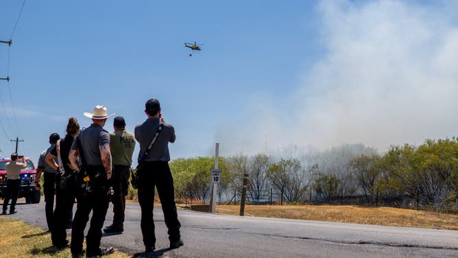 Austin, Texas Continues To Cope With Prolonged Heat Wave HAYS COUNTY, TEXAS - AUGUST 08: Members of the Hays County Emergency Service Districts and the Kyle and Buda Fire Departments look on as a helicopter prepares to drop water on a wildfire during an excessive heat warning on August 08, 2023 in Hays County, Texas. The city of Austin and its neighboring counties continue to grapple with a prolonged heat wave, with excessive heat advisories being issued across the state. (Photo by Brandon Bell/Getty Images)