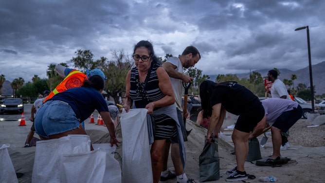 PALM SPRINGS, CA - AUGUST 19, 2023: With storm clouds looming overhead, Bernadette Duran of San Gabriel carries sandbags to protect her vacation home from predicted flooding from Hurricane Hilary in Palm Springs on August 19, 2023 at City Hall in Palm Springs, California.