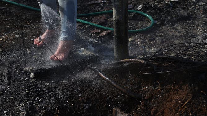A resident, who did not giver her name, uses a garden hose to cool her feet after stepping hot embers at a neighbor's house that was destroyed by wildfire on August 12, 2023 in Kula, Hawaii.