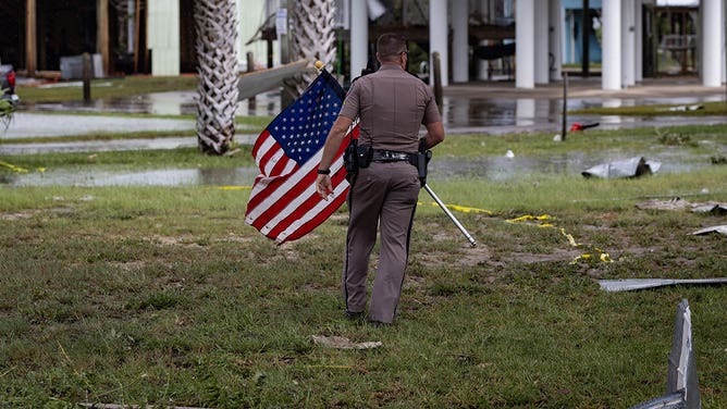 A sheriff's deputy picks up an American flag from debris following Hurricane Idalia in Horseshoe Beach, Florida, US, on Wednesday, Aug. 30, 2023.