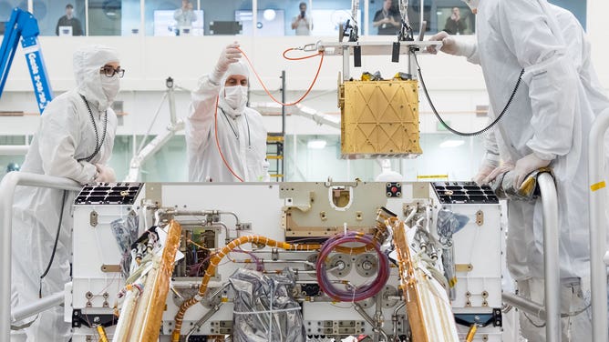 Members of NASA’s Mars 2020 project install the Mars Oxygen In-Situ Resource Utilization Experiment (MOXIE) into the chassis of NASA’s Mars rover on March 20, 2019 in the Spacecraft Assembly Facility’s High Bay 1 Cleanroom at NASA’s Jet Propulsion Laboratory, in Pasadena, California.