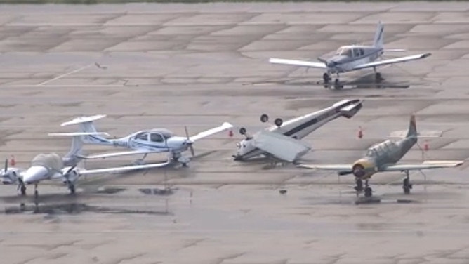 An upturned plane in the middle of other small planes on the tarmac.