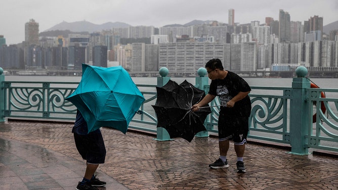 People struggle with their umbrellas in high winds brought by Super Typhoon Saola next to Victoria harbour in Hong Kong on September 1, 2023.