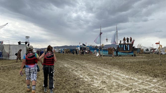 TOPSHOT - Attendees walk through a muddy desert plain on September 2, 2023, after heavy rains turned the annual Burning Man festival site in Nevada's Black Rock desert into a mud pit. Tens of thousands of drenched festivalgoers were stranded on September 3, 2023, in deep, sticky mud in the Nevada desert after torrential rain turned the annual Burning Man gathering into a quagmire. All events at the counterculture festival, which drew some 70,000 people, were canceled after rain tore down structures for dance parties, art installations and other eclectic entertainment.